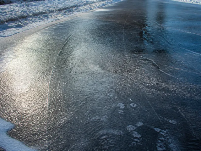 Spiegelglatte schwarze Eisfläche auf einem Weg als Symbol für erneutes Gefrieren nach Tauwetter
